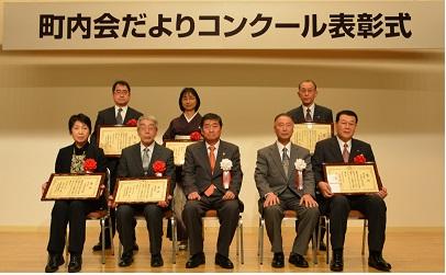 男女8人の受賞者たちが賞状を手にして写る町内会だよりコンクール表彰式の記念写真