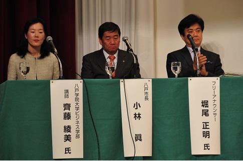 緑色の布が貼られたテーブルに座る地域活動についてスピーチをする3人の地域活動関係者の写真