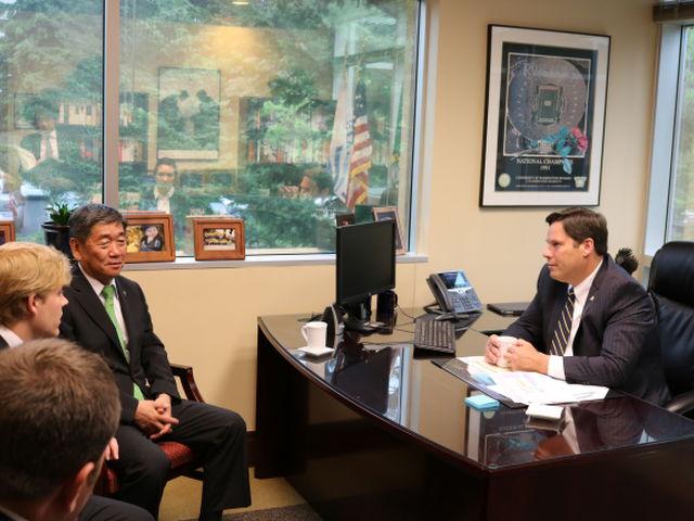市長室で自身のデスクに座る市長とその前に座る八戸市市長らの訪問時の写真
