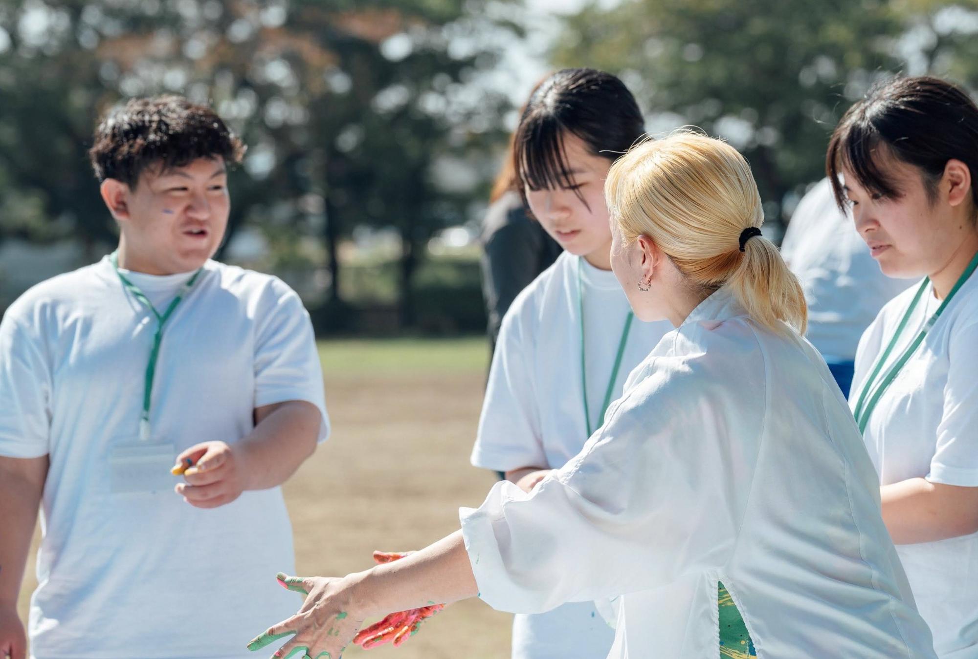 講師が高校生の参加者に指導を行っている様子。緑の背景の中、楽しそうに話う合う姿が見える。