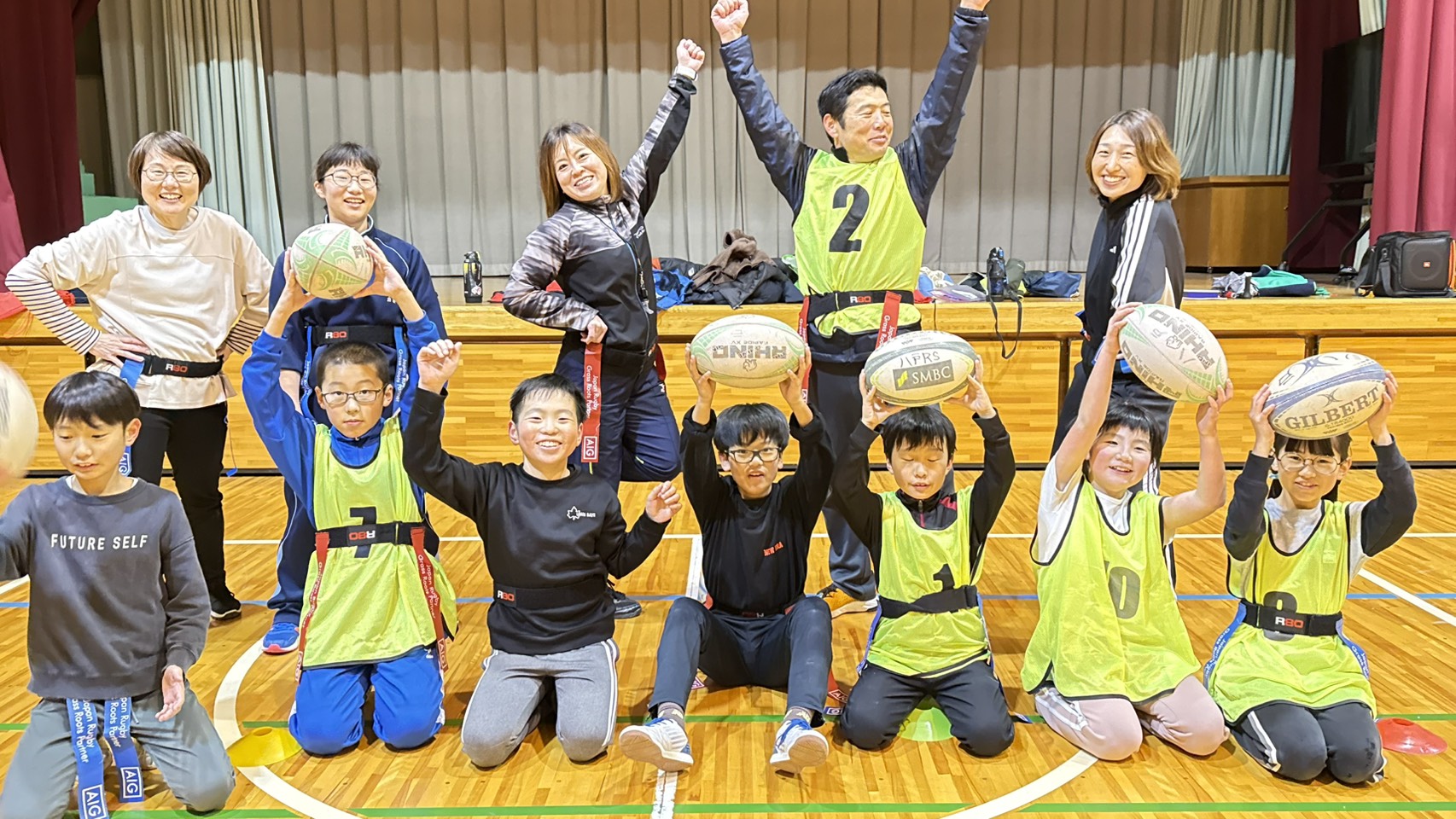 子どもたちと指導者が明るい表情で、バスケットボールを持ちながらポーズを決めている姿。体育館での活動風景。