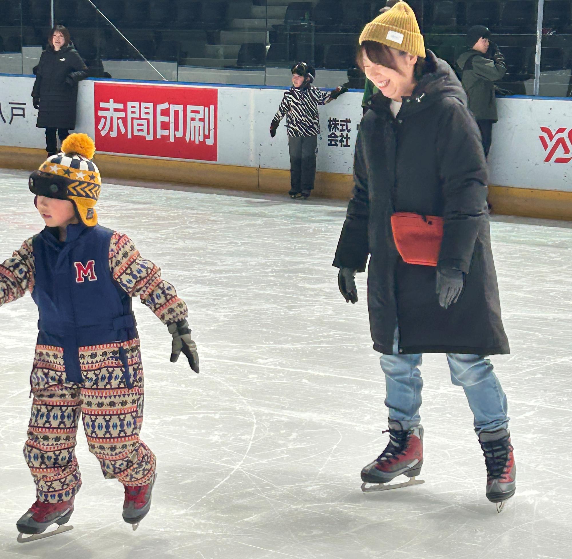 親と一緒にアイススケートを楽しむ子ども。カラフルな複素で、笑顔を浮かべながら滑っている様子が写っている。