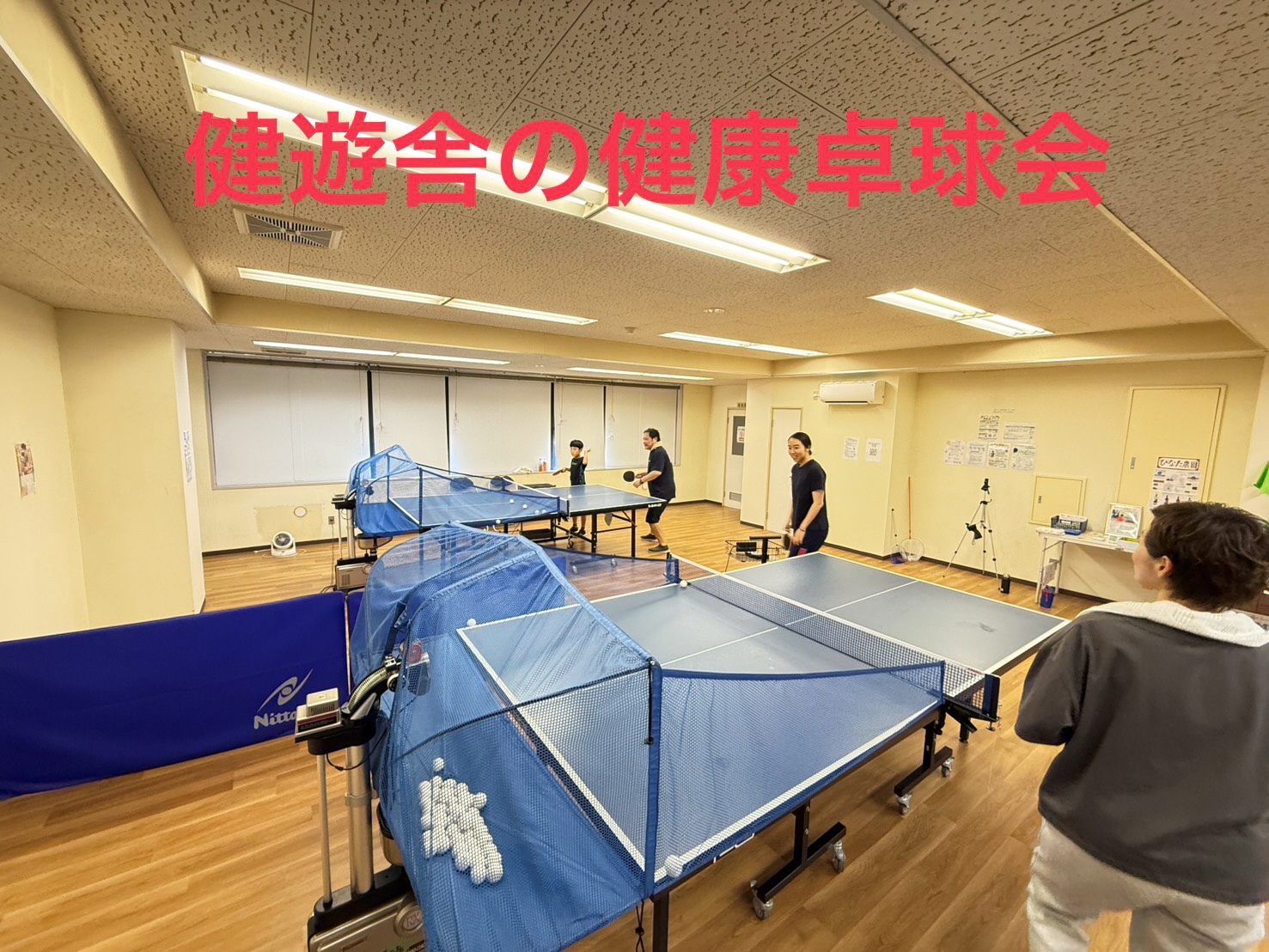 卓球台が設置された室内で、参加者が真剣な表情で卓球を楽しんでいる様子。健康促進を目的とした卓球界の風景。