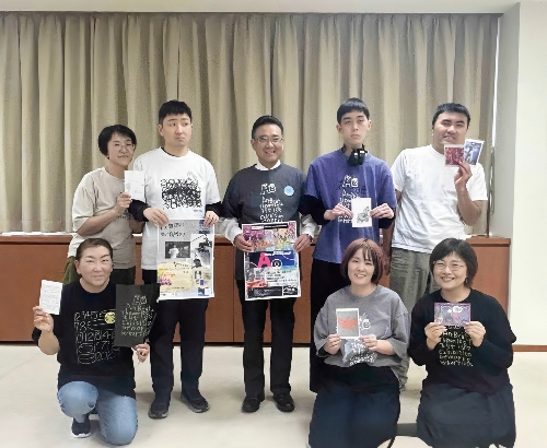 市長と8名のメンバーが笑顔で集まっている。各自が手にアート作品のサンプルや告知を持っている。