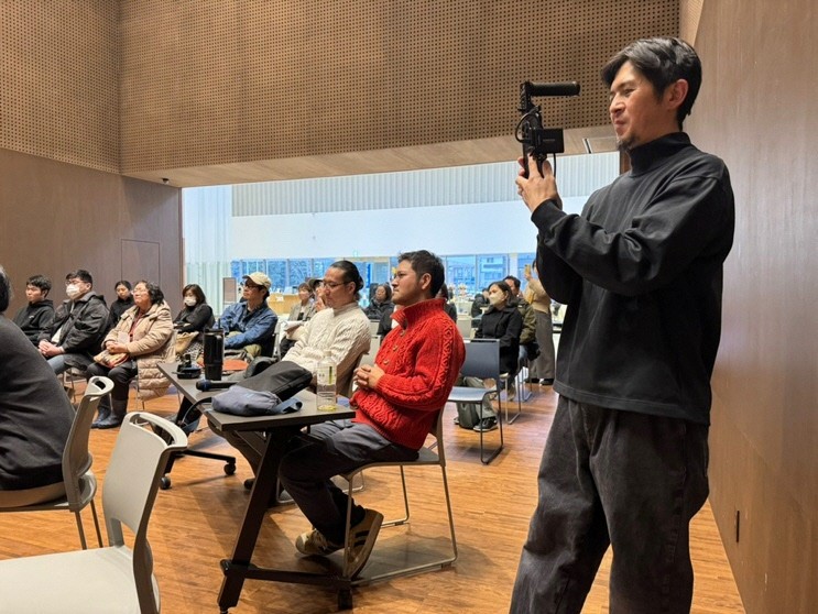 会場で講演を聴き、記録撮影する参加者と座席の様子