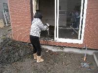 赤いレンガの外壁の家から津波によって屋内に蓄積した泥を屋外へ窓から書き出している灰色のジャケットを着た女性の写真