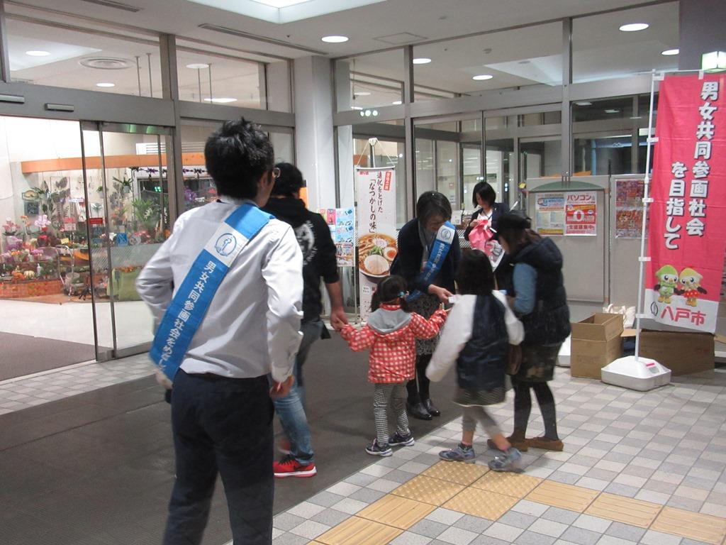 手前にたすきをかけた男性、奥に子供2名、大人2名の家族にティッシュを渡しているたすきをかけた女性の写真