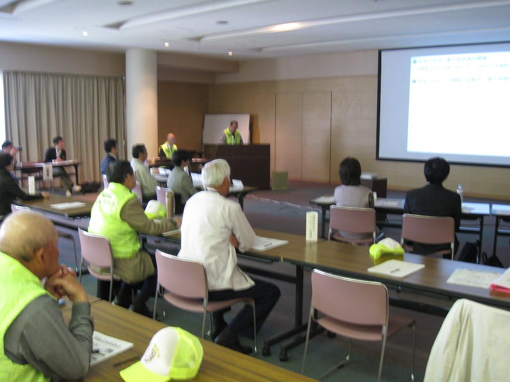 会議室でスクリーンに映し出される活動結果のスライドを見る参加者らを会場後方から写した写真