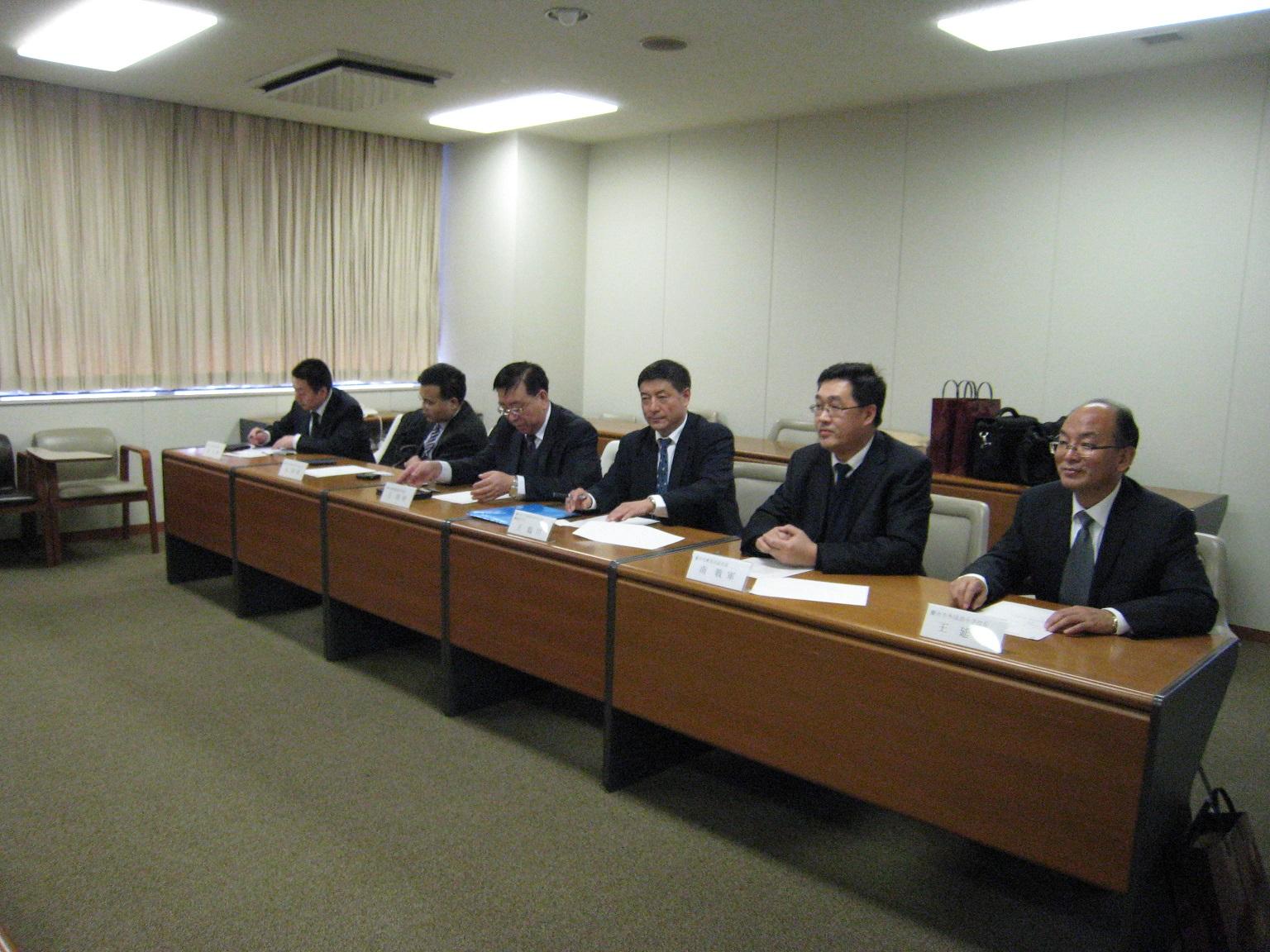 6人のスーツ姿の男性が一列で机に向かい座っている写真。