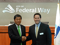 小林眞市長とフェデラルウェイ市市長がフェデラルウェイ市の看板の前で握手している写真