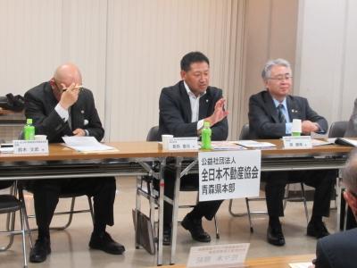 左に頭を抱えて座っている男性、中央で座って手を上げて話をしている男性、右に座って話を聞いている男性の写真