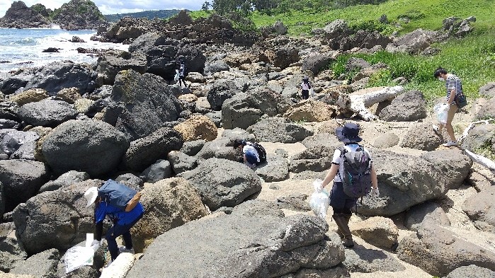 海岸岩場で大きな岩の隙間のごみを拾うメンバー