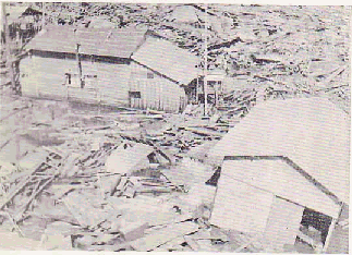 漁港等の状況・倉庫のような建物2棟がありその周りに崩れた瓦礫が一面を覆っている写真