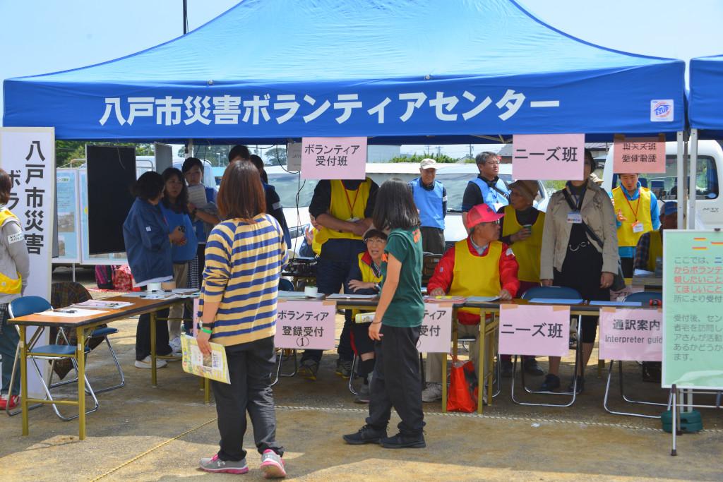 八戸災害ボランティアセンターと書かれたテントに集まっている人々の写真