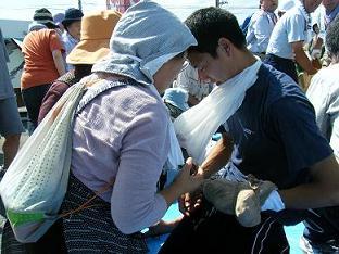 女性が男性に白い腕つり用の三角巾をつけて救護訓練をしている写真