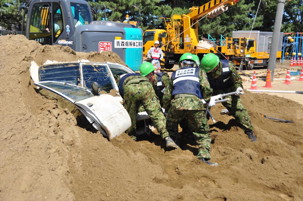 4名の自衛隊員が土に埋まった車から救助する訓練をしている写真