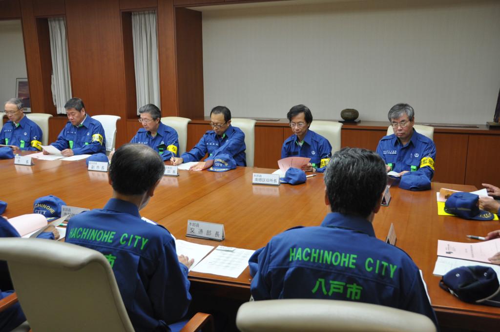 青い服を着た消防隊員の方々が会議をしている写真