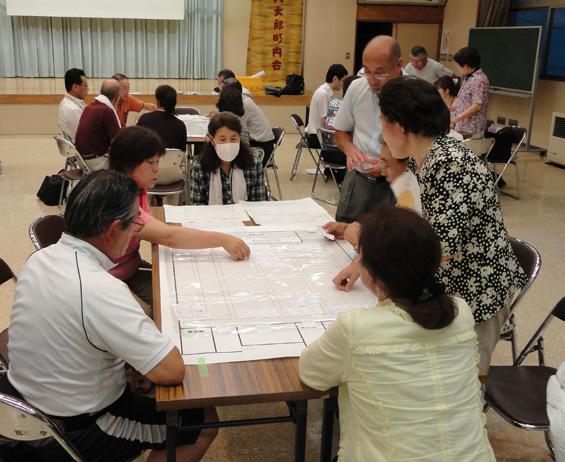 机に6人ほどのグループに分かれ避難所の地図を広げて避難所運営ゲームをしている市民の写真