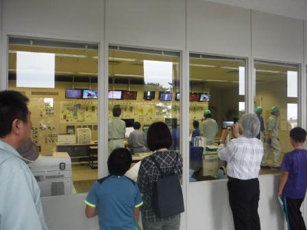 ガラス越しにモニターや大きなコントロールパネルが設置されている中央制御室を見ている参加者たちの写真