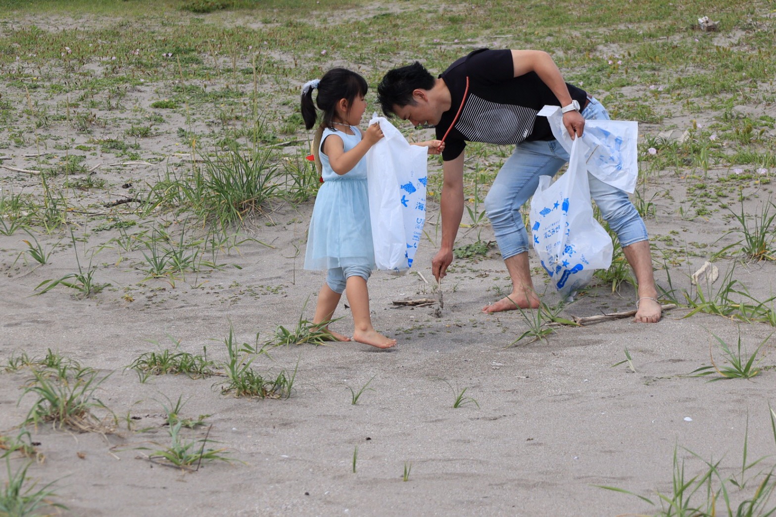 砂浜で海ごみウィークのごみ袋を手にごみを拾う父親と娘