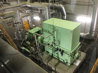 緑色の箱状の機械や大きな鉄製の管などで出来ている蒸気タービン・発電機の写真