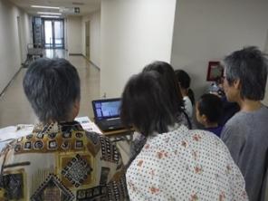 見学に参加している子ども達や女性達が、パソコンの画面を興味深く見入っている様子の写真