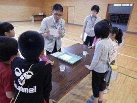 体育館で講師の先生の話を聞いている小学生の写真