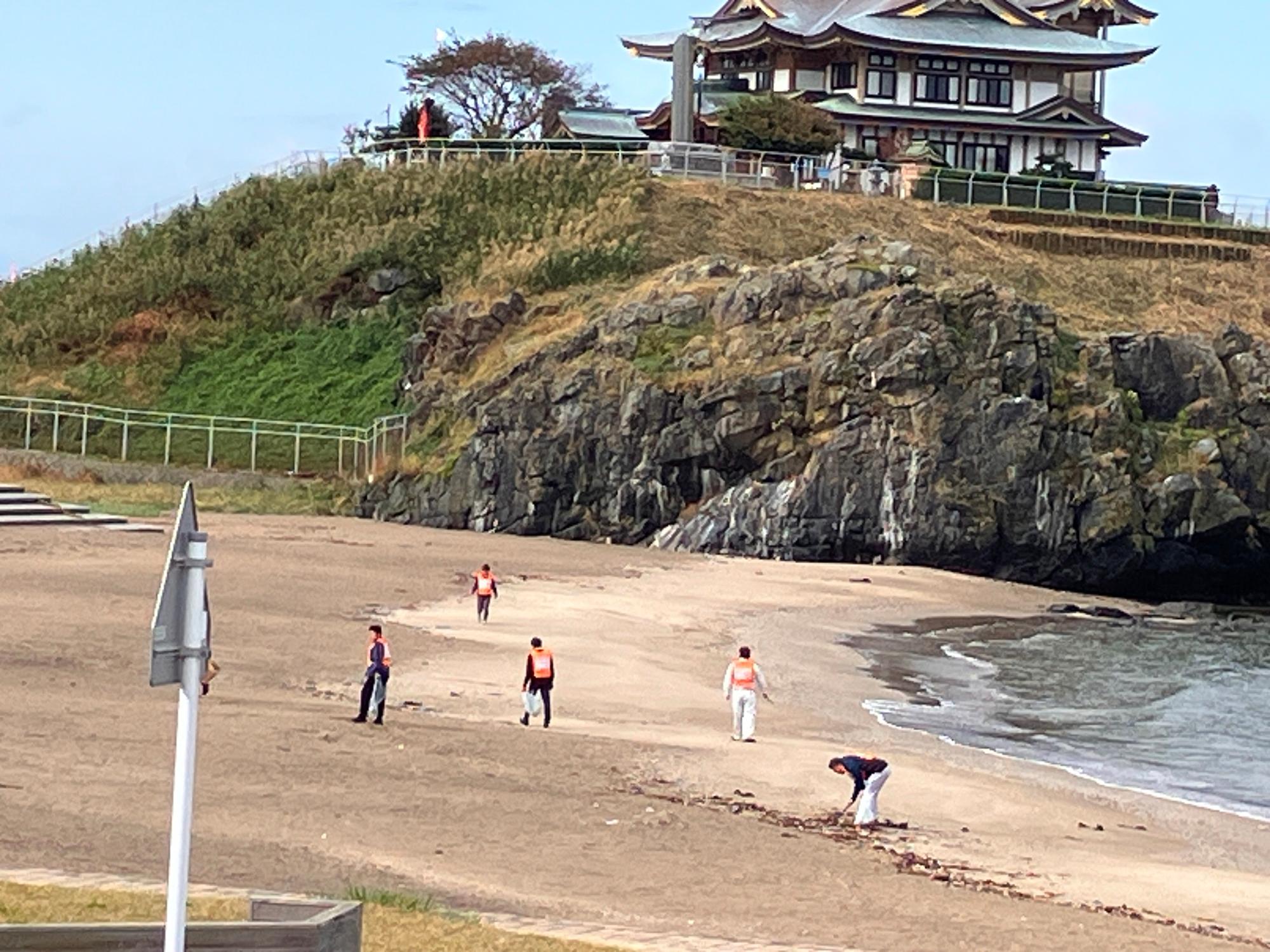 蕪嶋神社の見える砂浜でごみを拾う人たちの写真