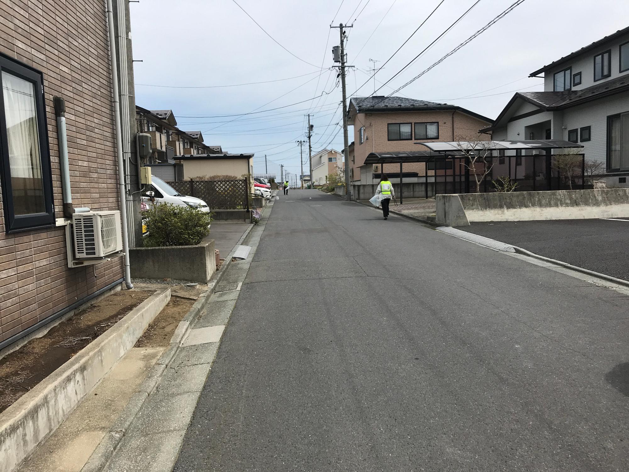 住宅地の広い道路でごみを拾う一人の社員