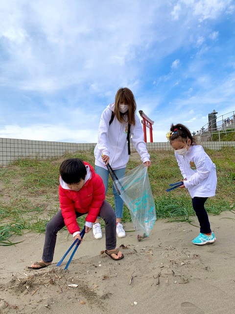 蕪嶋神社の鳥居をバックに砂地のごみを拾う親子の写真