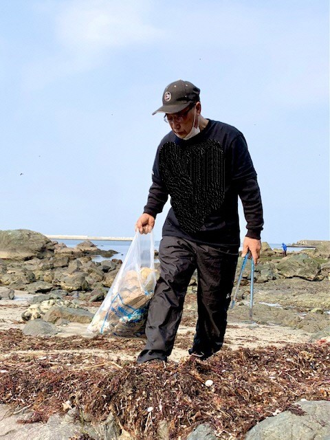 岩場を歩きながら、片手にトング、片手にごみ袋を持ち活動している男性の写真