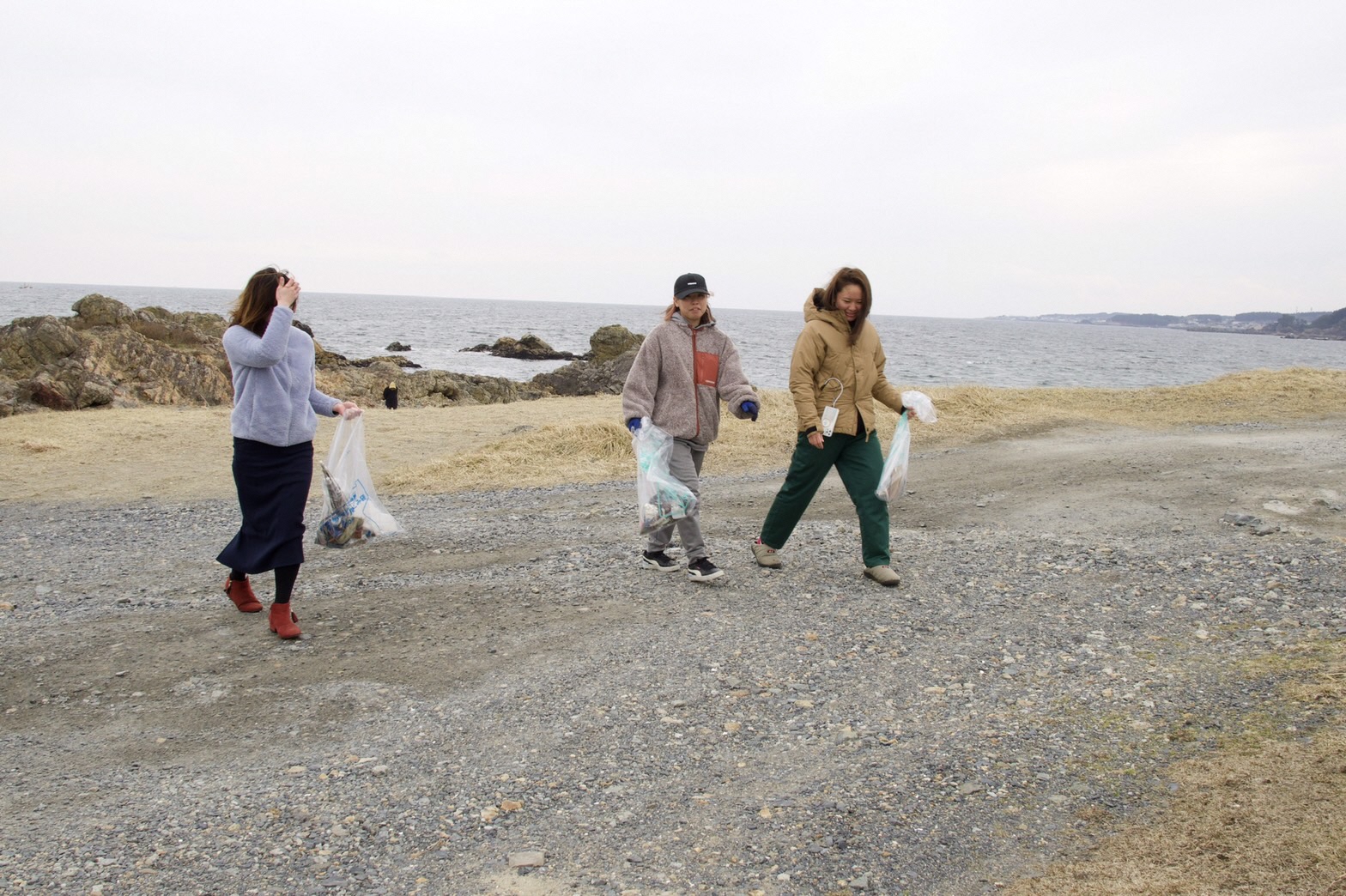 海岸のごみを入れたボランティア用ごみ袋を持って歩く女性3人の写真