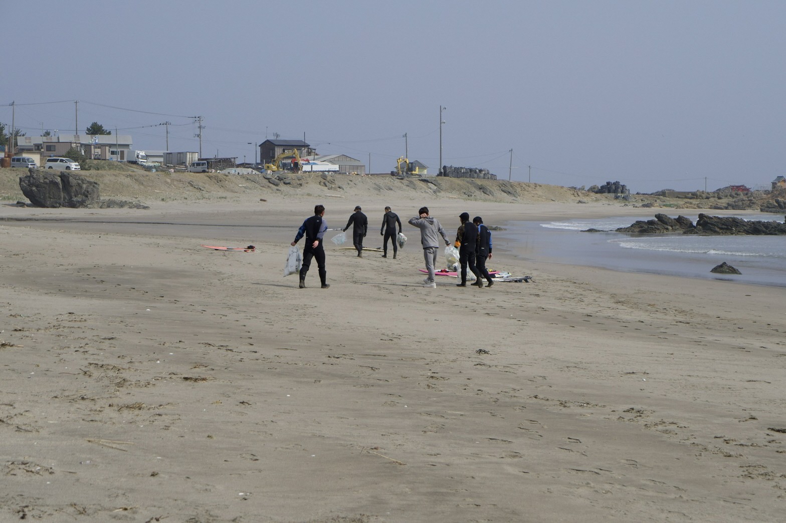 波打ち際の砂浜をボランティア用ごみ袋を手に歩く6人の写真