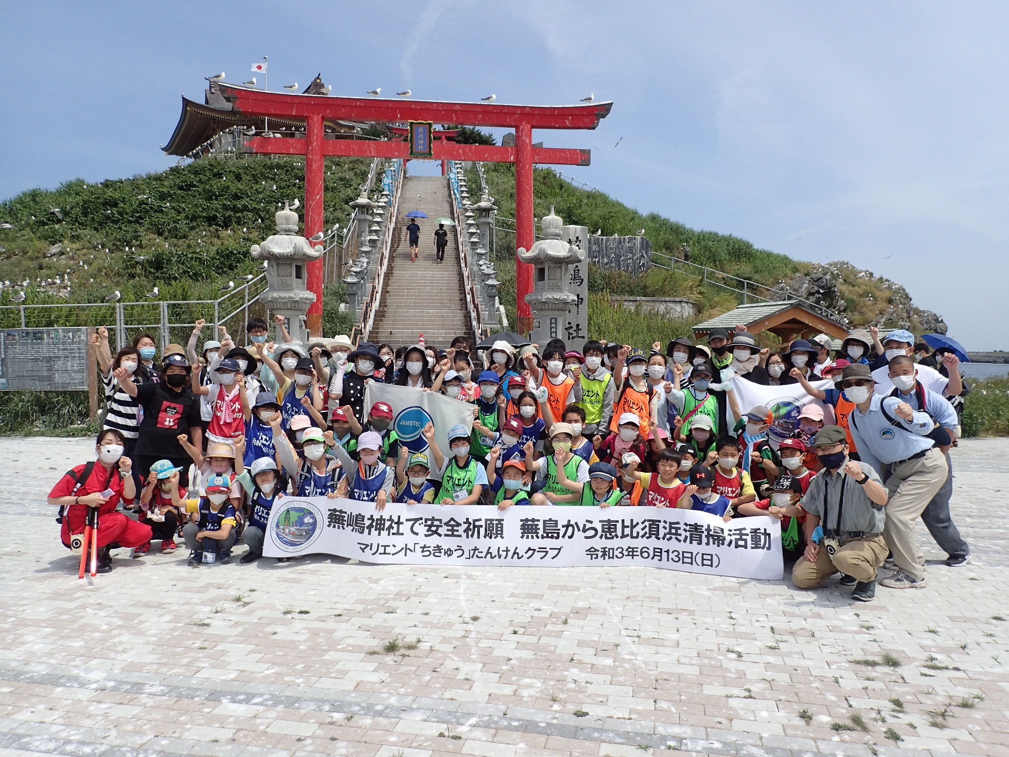 蕪島神社鳥居前で横断幕を広げ集合写真に写る87人のメンバー