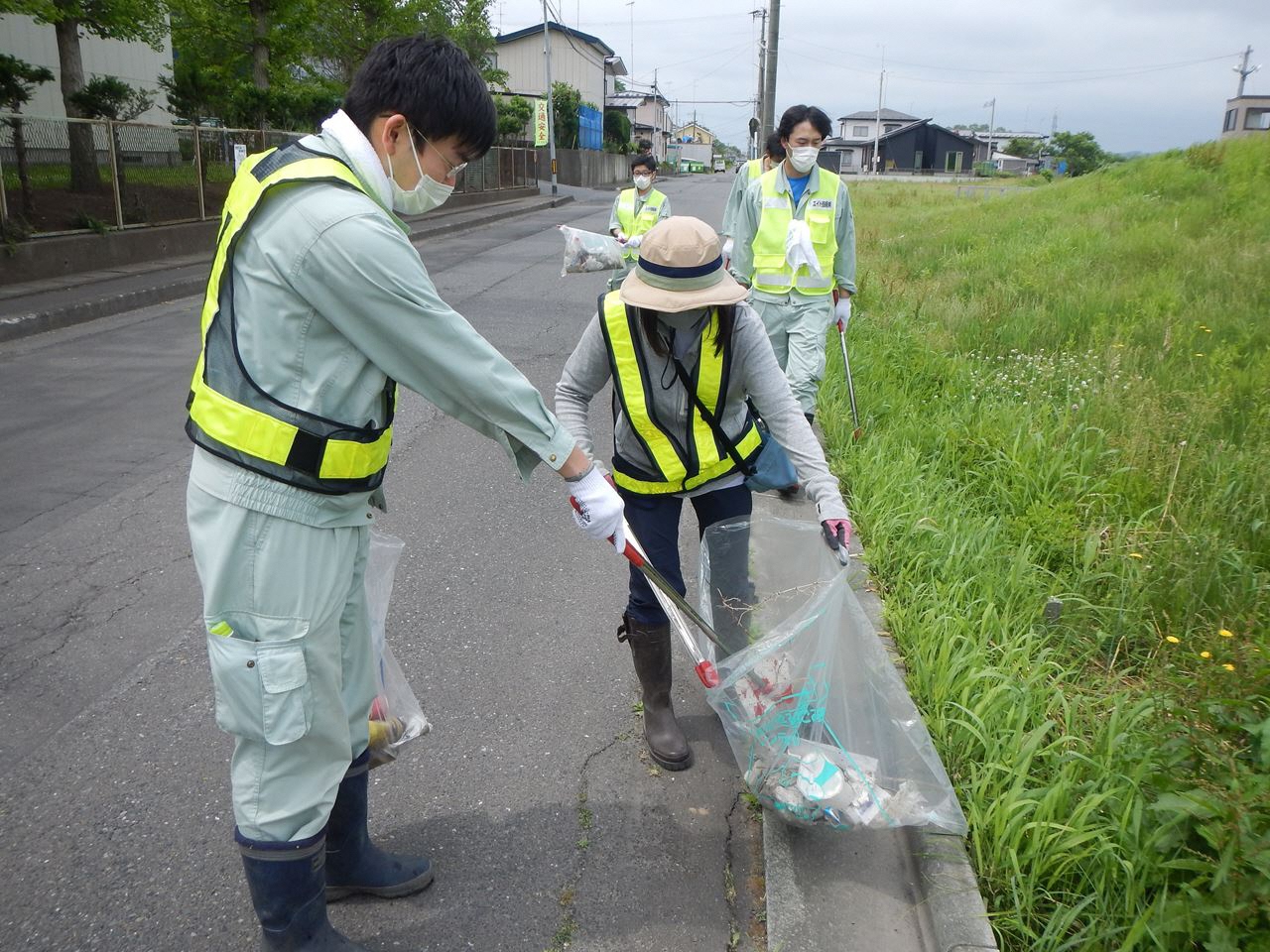 ごみ袋の口を広げる人、拾ったごみをトングでそれに入れる人