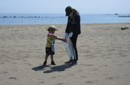海に近い砂浜のごみを拾う3歳くらいの子どもと女性