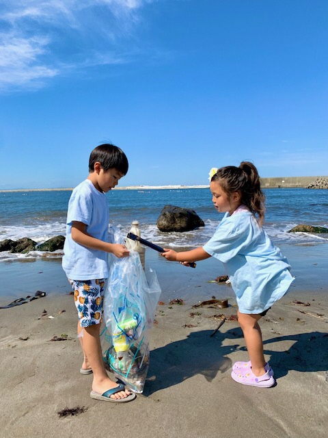 海岸でトングで拾ったごみをボランティア用ごみ袋に入れるこどもふたり