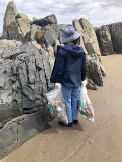 海岸岩場で集めたごみの入ったボランティア用ごみ袋を両手に持つ女性ひとり