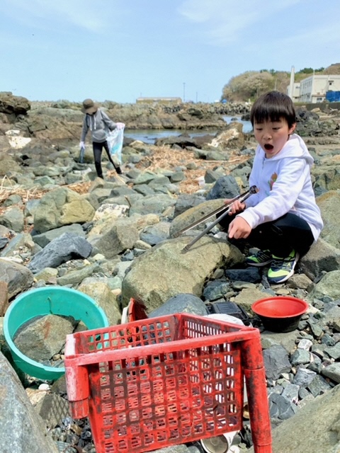 岩場に打ち上げられたプラスチックごみを集める子供の写真