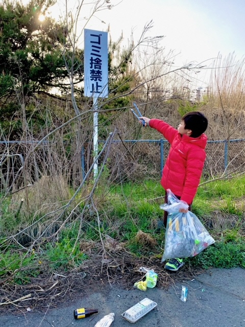 ゴミ捨て禁止の看板を指し示し、その下のごみを拾う男の子の写真