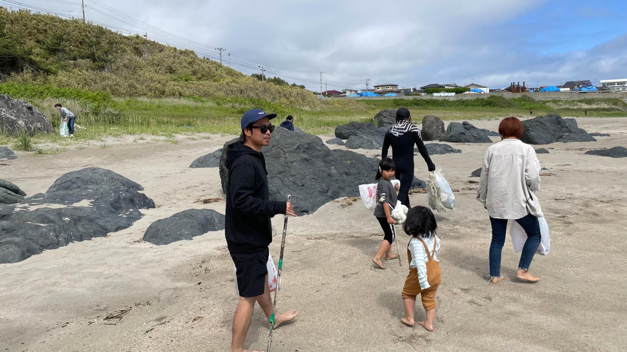 小さな子供達と一緒に砂浜でごみを見つけている人たちの写真