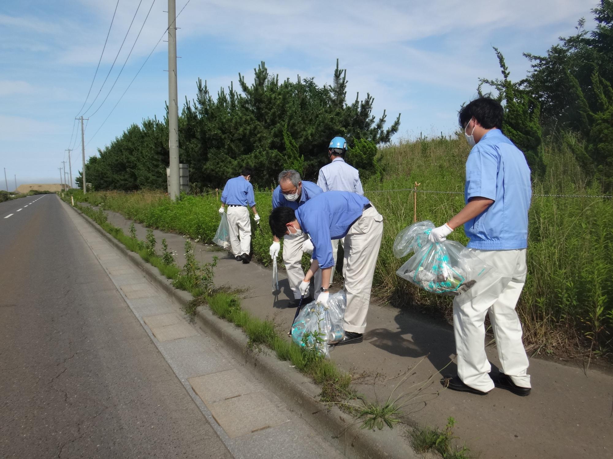 歩道を歩きながらボランティア用ごみ袋を手に、ごみを拾っている写真