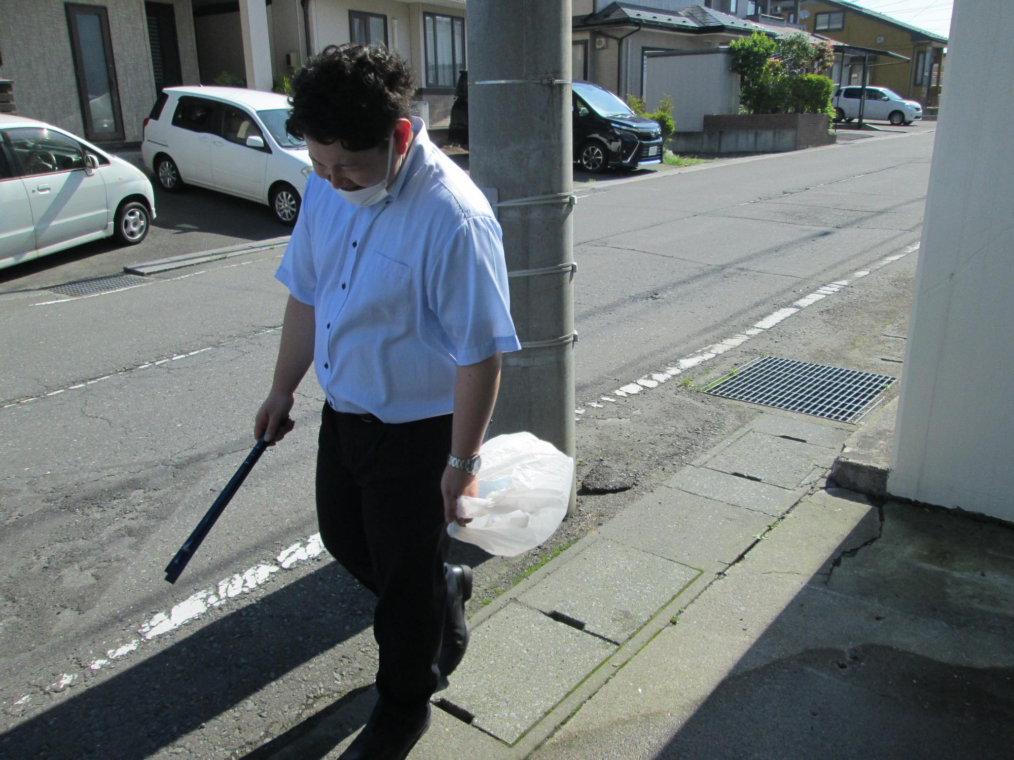 トングとごみ袋を手に持ち、歩道で活動する男性の写真