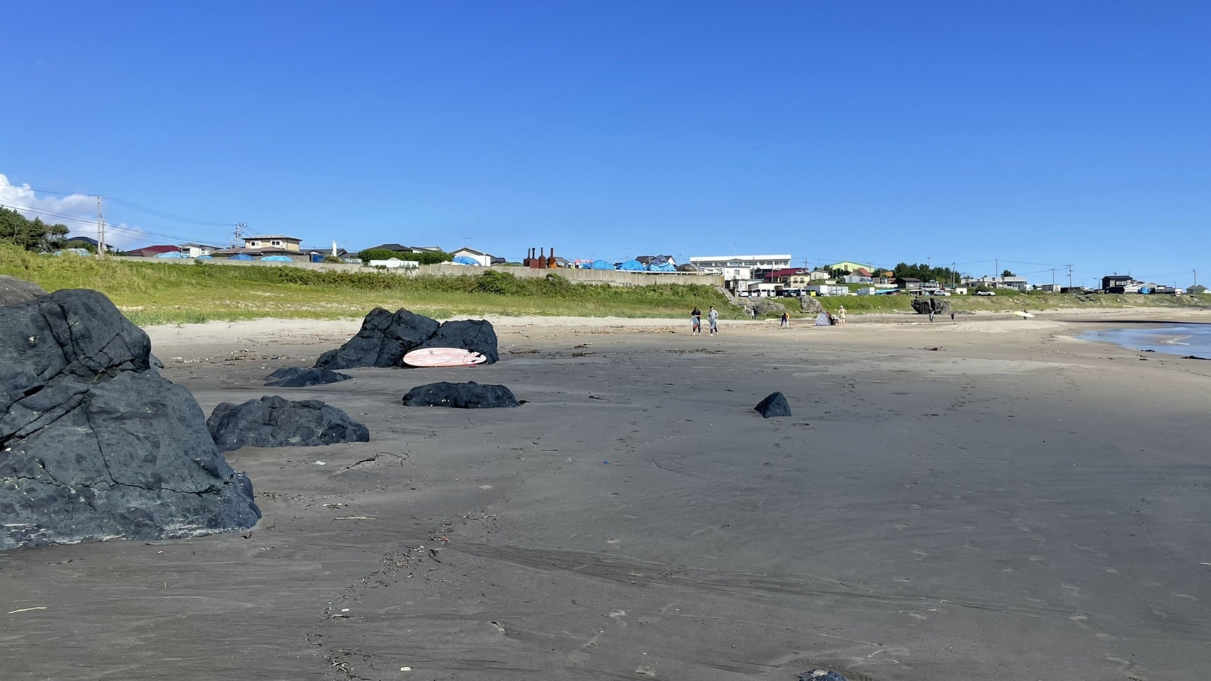 大きな岩のある砂浜で活動するサーファーたちを遠くから写した写真