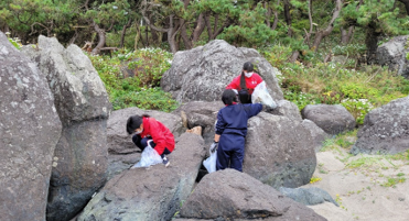 大きな岩に乗った生徒とその下でごみを探す二人の写真