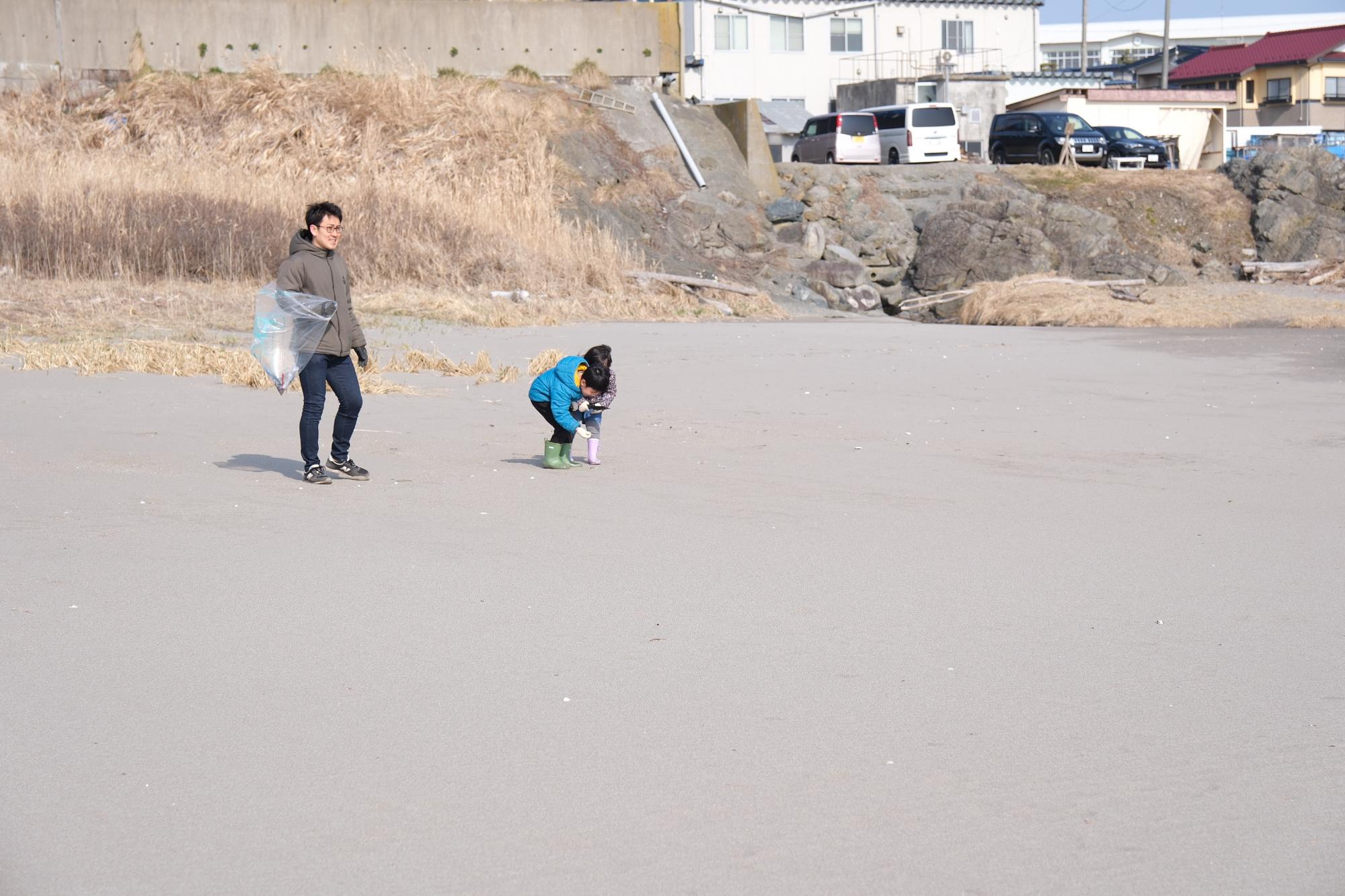 砂浜でごみを拾っている子供二人と男性の写真