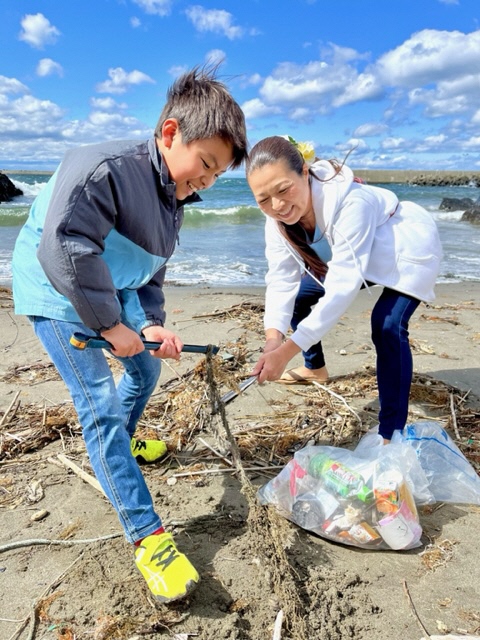 男の子と女性が砂浜で、砂に埋もれたごみを拾っている写真