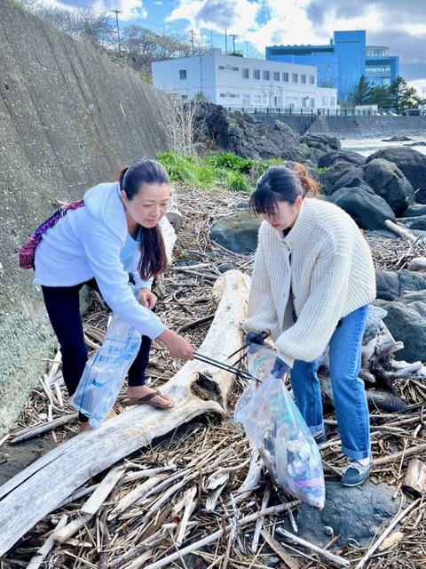 後ろに遠くマリエントが見える岩場で、女性二人がトングでごみを拾っている写真