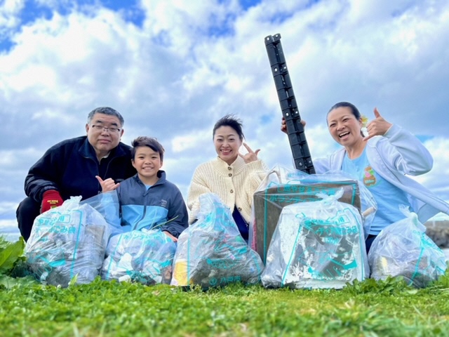 回収したごみを前に、青空をバックに4人で集合写真