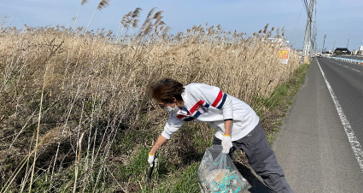 道路脇の草むらにポイ捨てされているごみを、腕を伸ばしてトングで拾っている一人の写真